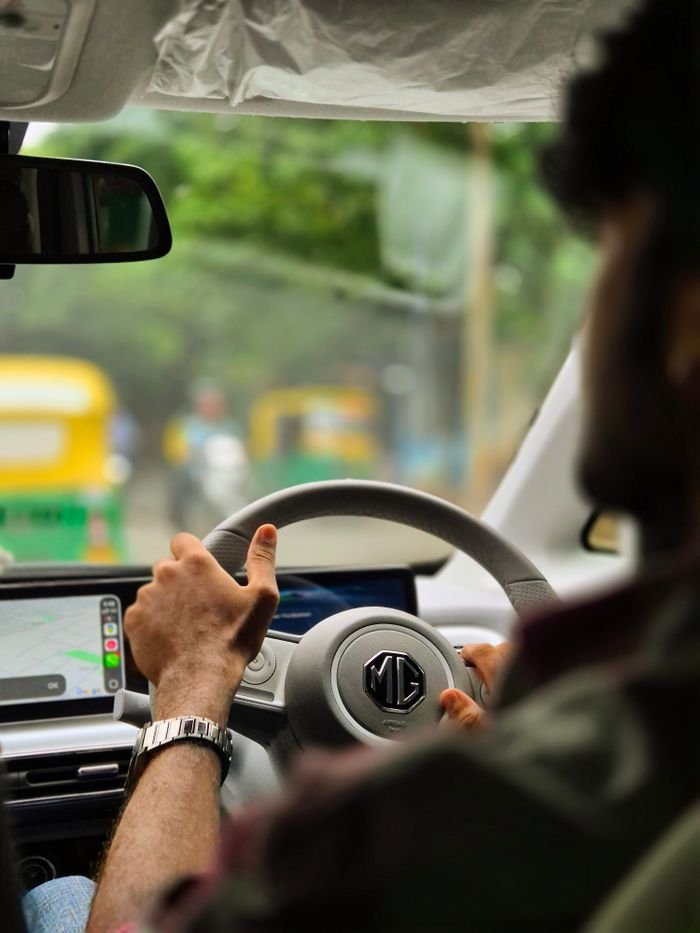 Man steering car in Bengaluru, India, navigating bustling urban traffic with auto-rickshaws.